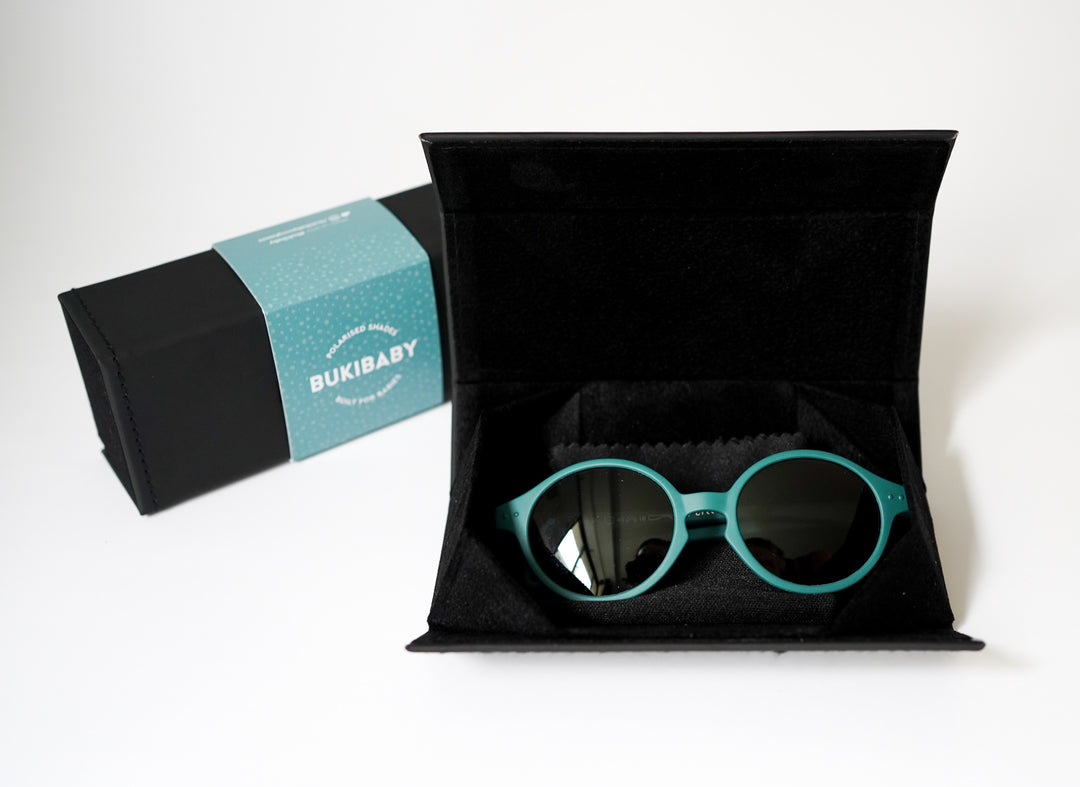 A pair of blue Bukibaby Sunglasses in their black carrying case.