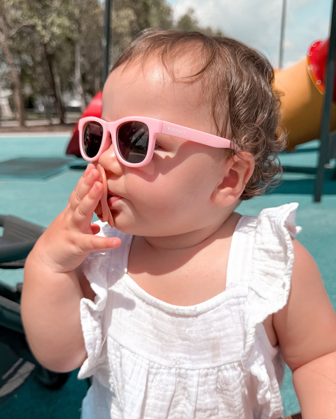 Baby wearing pink sunglasses at a playground